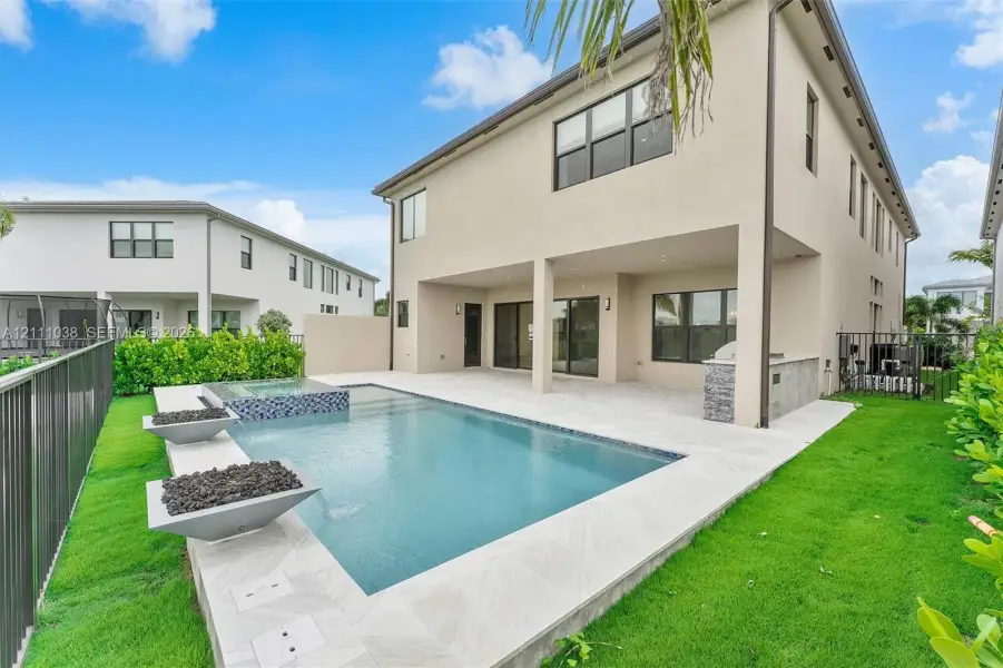 Outdoor living space featuring a covered patio, built-in stone-finish grill station, swimming pool with integrated spa, and two spill-over water features