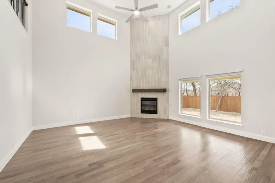 Open living room with two-story ceilings, tile fireplace surround, hardwood floors, and ceiling fan
