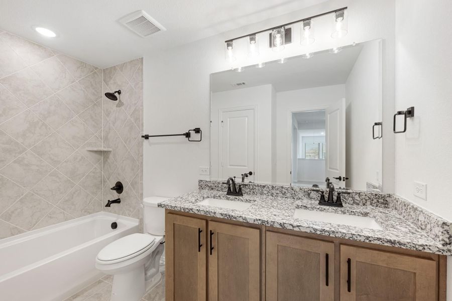 Bathroom with double sink vanity, granite countertop, wood cabinets, and tiled tub-shower combo with black fixtures. Bathroom with double sink vanity, granite countertop, wood cabinets, and tiled tub-shower combo with black fixtures.