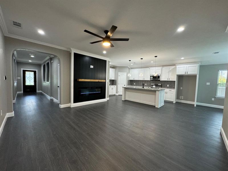 Unfurnished living room with dark hardwood / wood-style flooring, ceiling fan, and ornamental molding