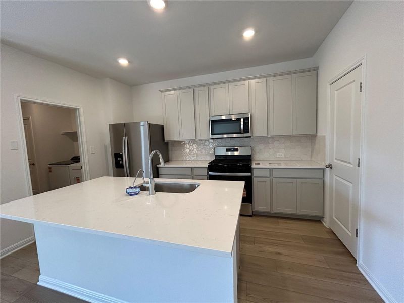 Kitchen featuring appliances with stainless steel finishes, decorative backsplash, dark wood-style flooring, light stone counters, and gray cabinets