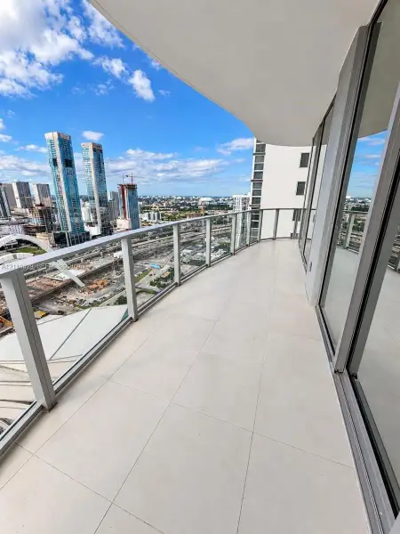 Covered private balcony featuring large-format tile flooring, a glass-panel railing, and floor-to-ceiling glass sliding doors