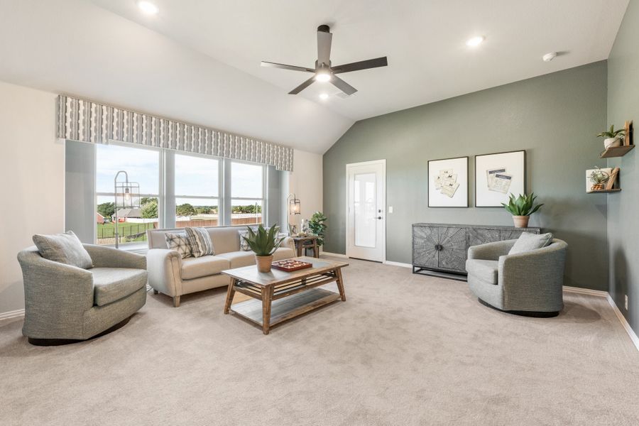 Living room with vaulted ceiling, ceiling fan, green accent wall, and large windows with carpet flooring