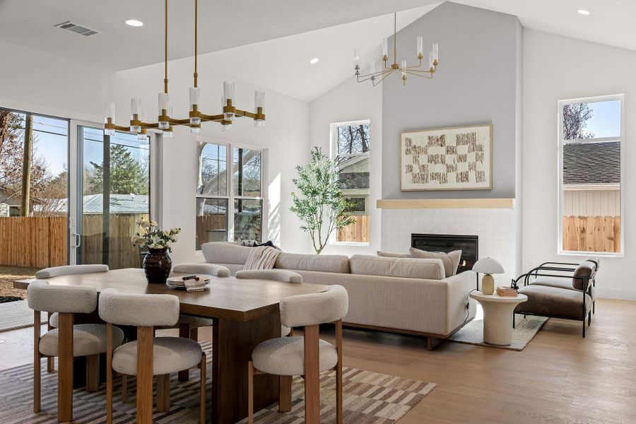 Dining area with suspended lighting, a high ceiling, a glass covered fireplace, and wood finished floors