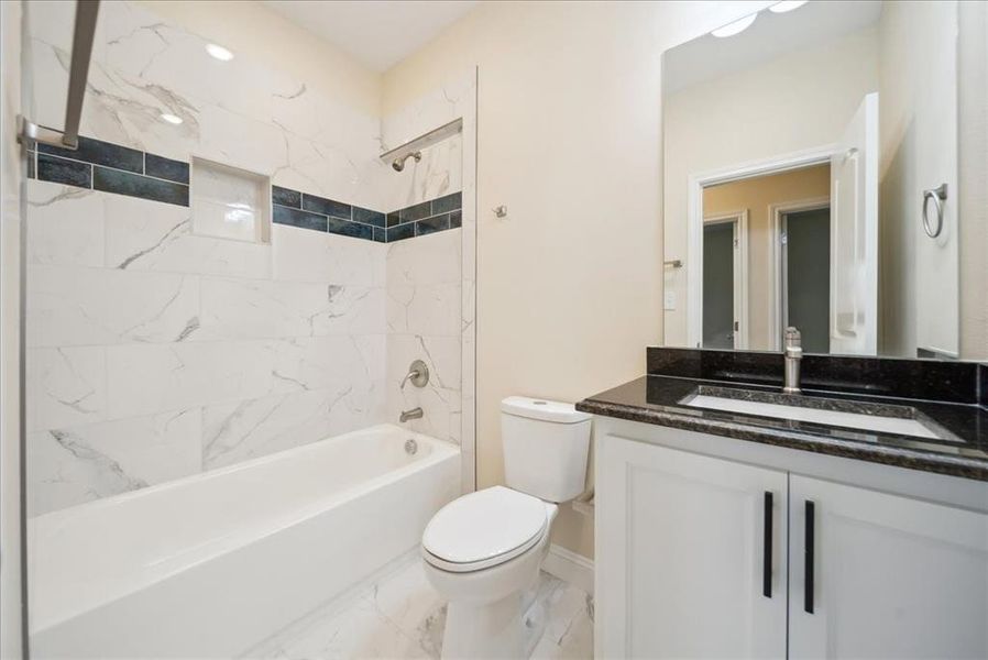 Full bathroom featuring vanity, tiled shower / bath combo, and toilet