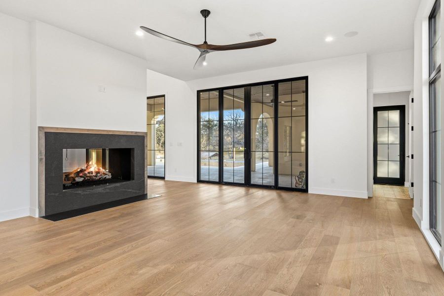 Unfurnished living room featuring a ceiling fan, a multi sided fireplace, light wood-style flooring, and recessed lighting