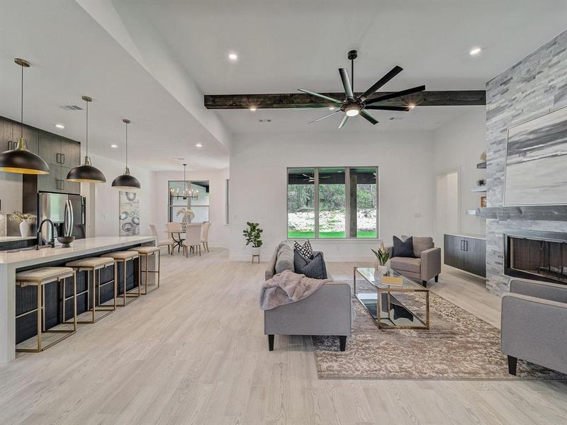 Living room featuring plenty of natural light, light wood-style floors, beam ceiling, a stone fireplace, and a ceiling fan