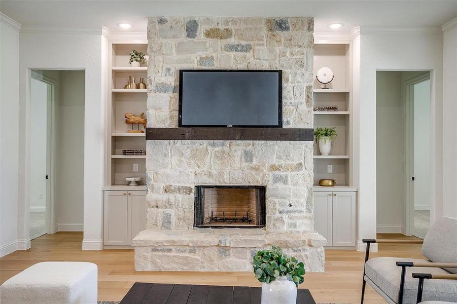 Living room featuring light hardwood / wood-style flooring, a stone fireplace, and crown molding