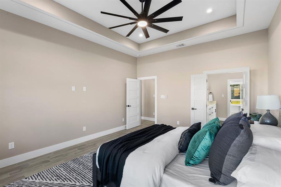 Bedroom with ceiling fan, light hardwood / wood-style floors, a raised ceiling, and ensuite bathroom