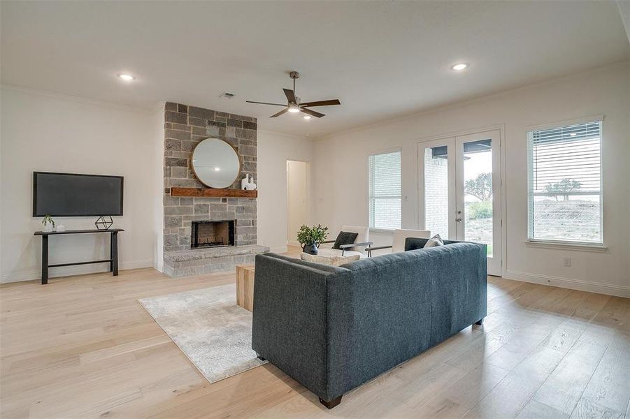 Living room with light hardwood / wood-style floors, a stone fireplace, and ceiling fan.