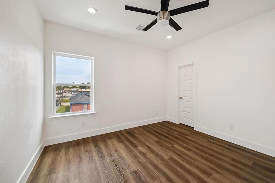 This inviting bedroom offers a clean, modern backdrop with warm wood-look flooring, bright white walls, recessed lighting, and a sleek ceiling fan. A large window fills the room with natural light and provides an elevated neighborhood view. The neutral finishes create a versatile canvas for a range of decorating styles, while the generous proportions and uncluttered layout make the space comfortable, functional, and ready to become a relaxing personal retreat. This inviting bedroom offers a clean, modern backdrop with warm wood-look flooring, bright white walls, recessed lighting, and a sleek ceiling fan. A large window fills the room with natural light and provides an elevated neighborhood view. The neutral finishes create a versatile canvas for a range of decorating styles, while the generous proportions and uncluttered layout make the space comfortable, functional, and ready to become a relaxing personal retreat.
