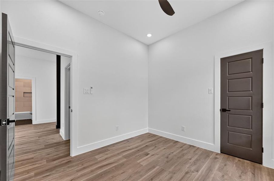Interior room with wood-finish flooring, white walls, recessed lighting, and a ceiling fan Interior room with wood-finish flooring, white walls, recessed lighting, and a ceiling fan