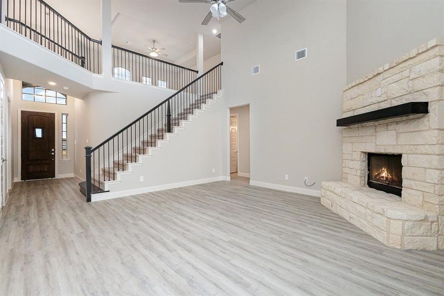 Unfurnished living room featuring ceiling fan, a stone fireplace, a towering ceiling, and light hardwood / wood-style flooring