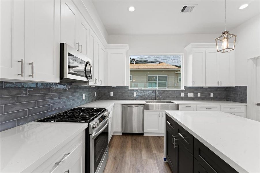 This modern kitchen features sleek white cabinetry, a stainless steel gas range, and a spacious island. The dark subway tile backsplash adds contrast, while the large window offers plenty of natural light.