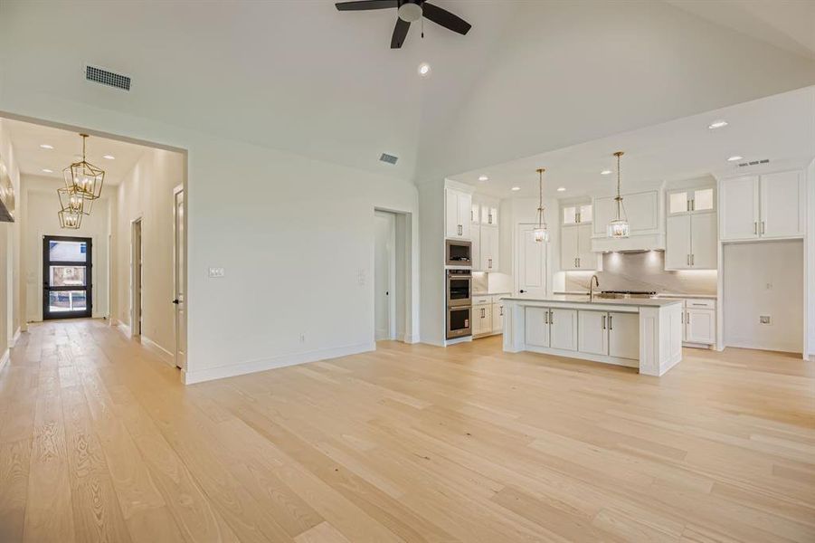 Unfurnished living room with recessed lighting, light wood-style flooring, high vaulted ceiling, a chandelier, and a ceiling fan Unfurnished living room with recessed lighting, light wood-style flooring, high vaulted ceiling, a chandelier, and a ceiling fan
