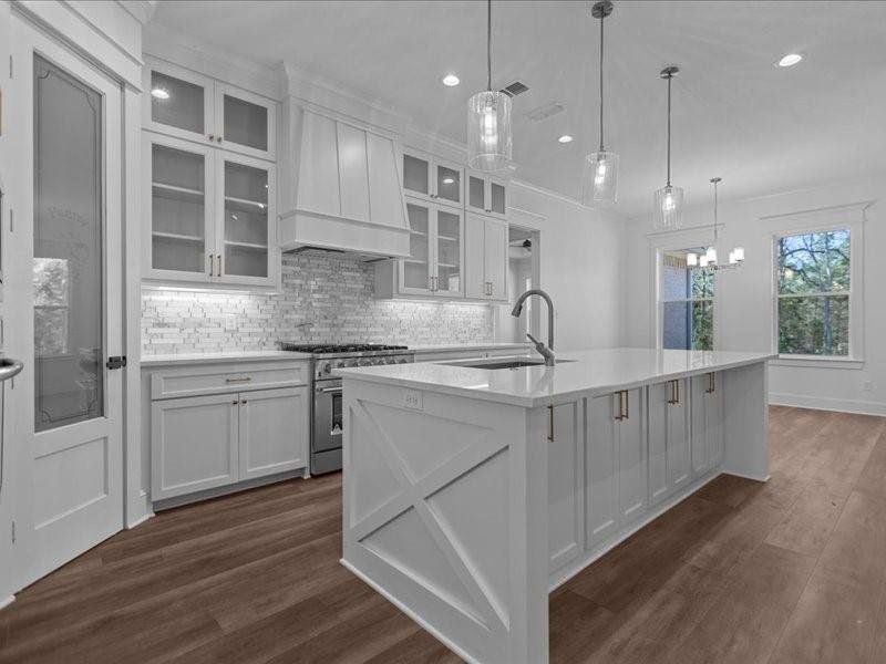 Kitchen with backsplash, white cabinetry, high end range, glass insert cabinets, and a kitchen island with sink