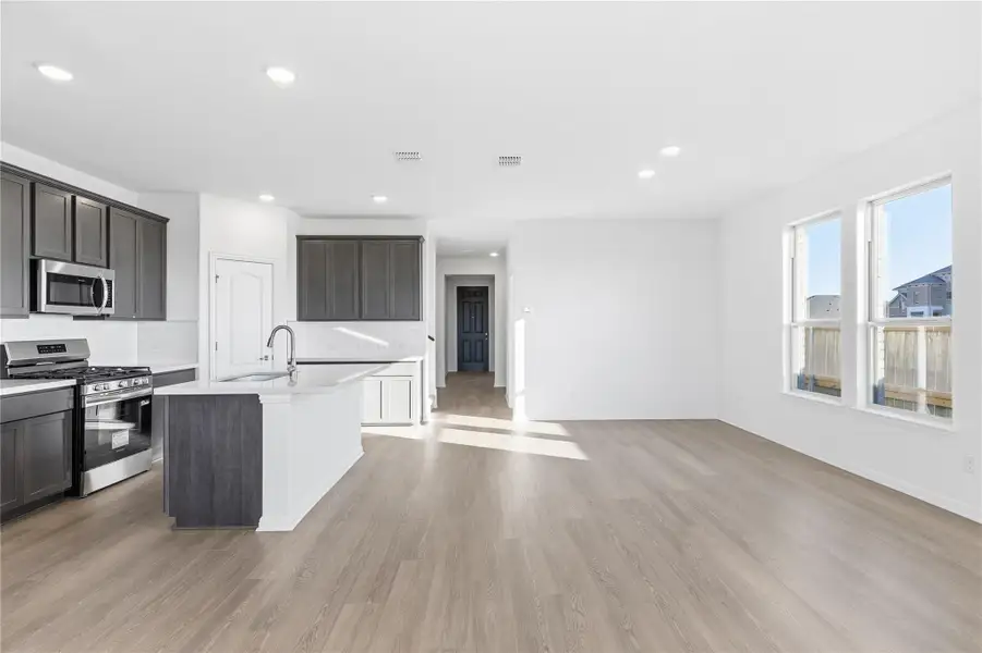 Kitchen featuring stainless steel appliances, backsplash, a kitchen island with sink, recessed lighting, and light wood-style flooring