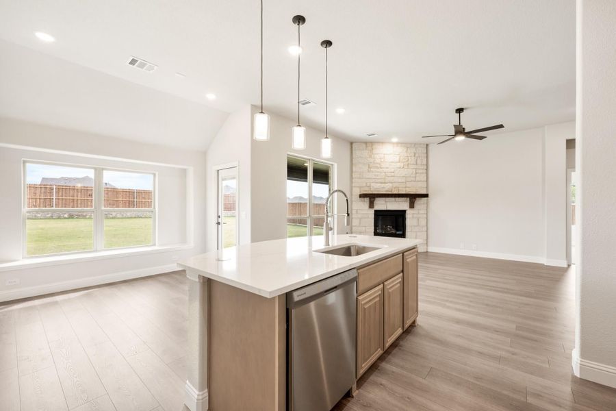 Kitchen island with sink and dishwasher, open to living room with stone fireplace and hardwood floors