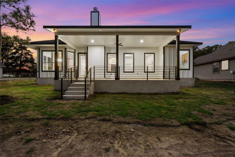 Back of property at dusk featuring a yard, a porch, and a ceiling fan
