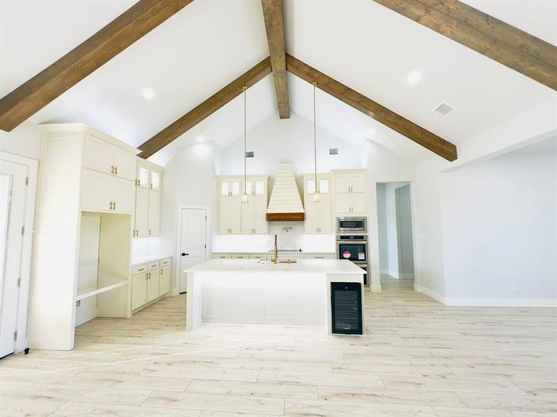 Kitchen featuring appliances with stainless steel finishes, custom range hood, a center island with sink, wine cooler, and hanging light fixtures