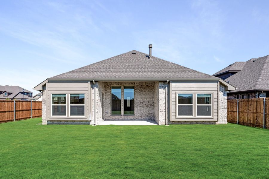Rear view of single-story brick home with covered patio, large windows, and fenced backyard with green lawn Rear view of single-story brick home with covered patio, large windows, and fenced backyard with green lawn