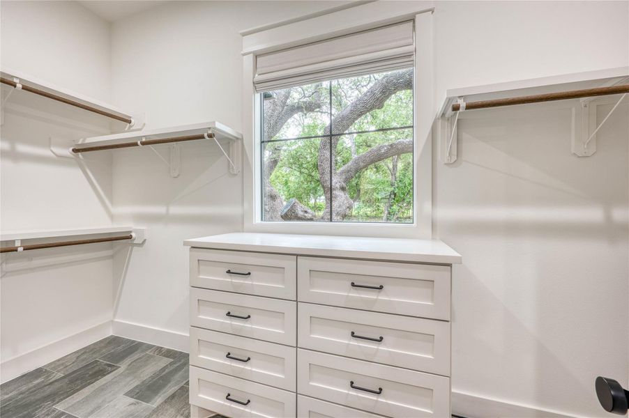 Walk-in closet featuring built-in shelving, white cabinetry with black hardware, a window with natural light, and wood-finish flooring