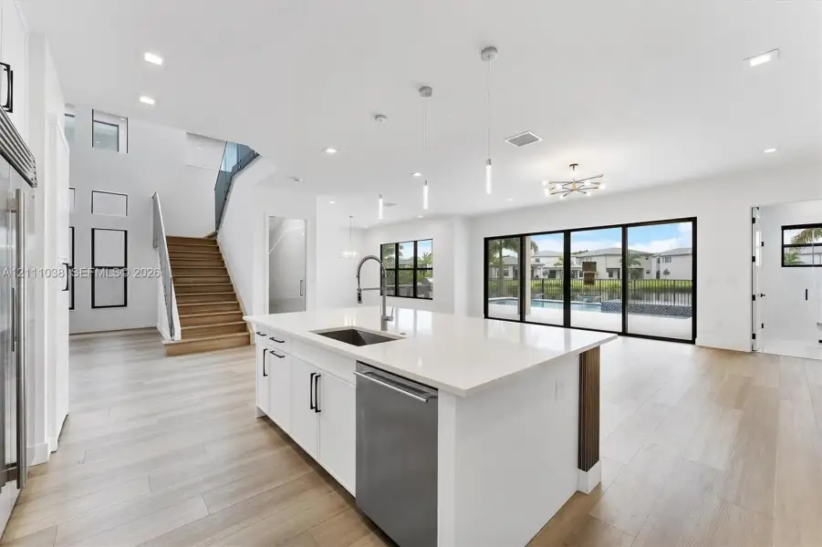 Open-concept kitchen featuring a center island with a quartz countertop, stainless steel dishwasher, and under-mount sink, complemented by wood-finish flooring, recessed lighting, and multi-panel sliding glass doors