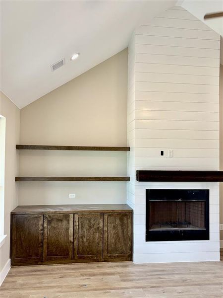 Unfurnished living room featuring vaulted ceiling, wood finished floors, a large fireplace, and recessed lighting Unfurnished living room featuring vaulted ceiling, wood finished floors, a large fireplace, and recessed lighting