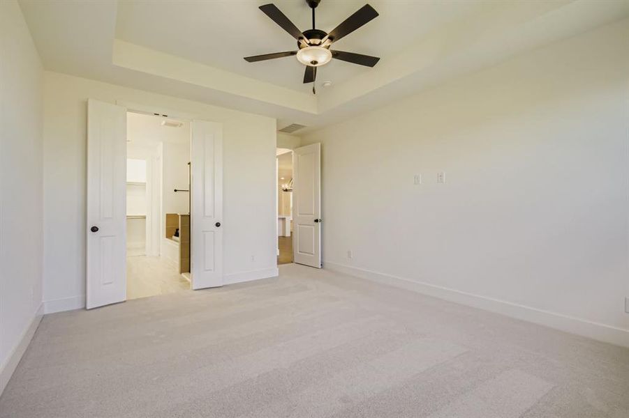 Unfurnished bedroom with light carpet, a raised ceiling, a ceiling fan, and connected bathroom Unfurnished bedroom with light carpet, a raised ceiling, a ceiling fan, and connected bathroom