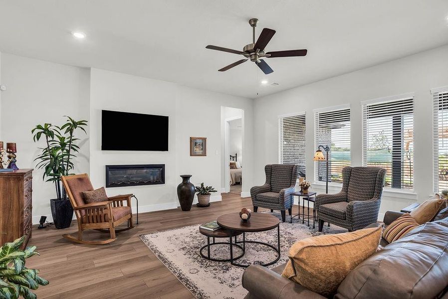 Open-concept living space featuring ceiling fan, ample natural light from multiple windows, an inset electric fireplace, and wood-finish flooring
