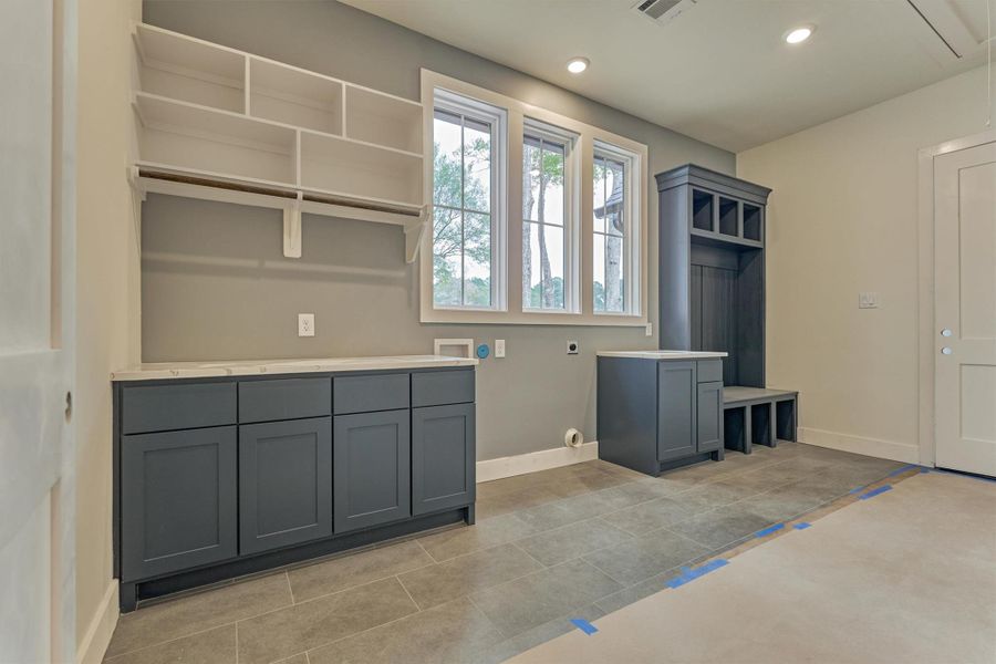 Stylish and functional laundry space featuring custom navy cabinetry, open shelving, and a built-in mudroom bench—all designed for everyday ease with a modern touch.