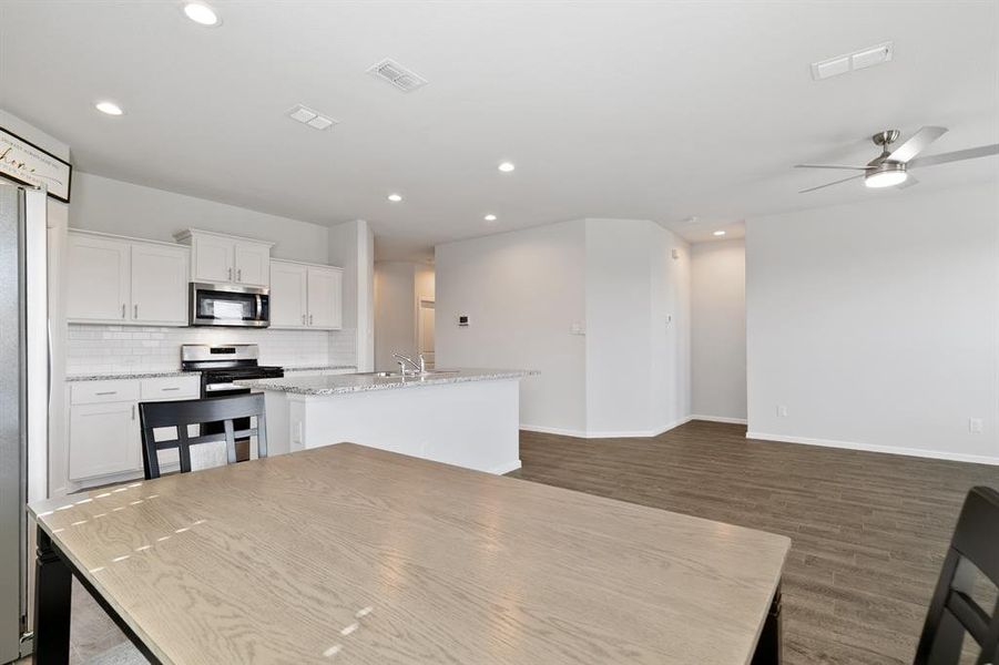 Kitchen with a center island with sink, backsplash, stainless steel appliances, white cabinets, and recessed lighting