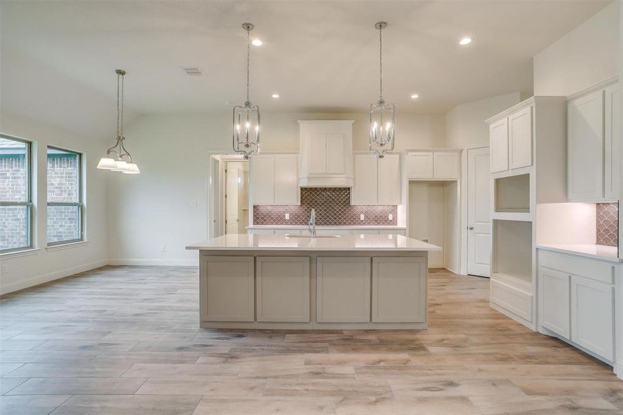 Kitchen featuring light hardwood / wood-style flooring, decorative light fixtures, and a kitchen island with sink