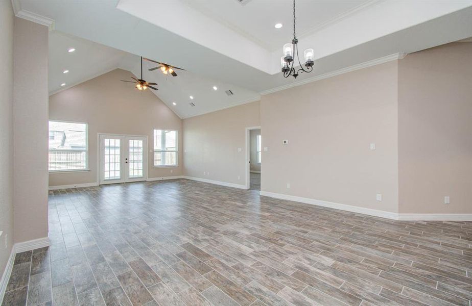 Spacious living area with high, vaulted ceilings, elegant wood-look tile flooring, abundant natural light from French doors and large windows, and modern light fixtures, offering a fresh canvas for personalization.