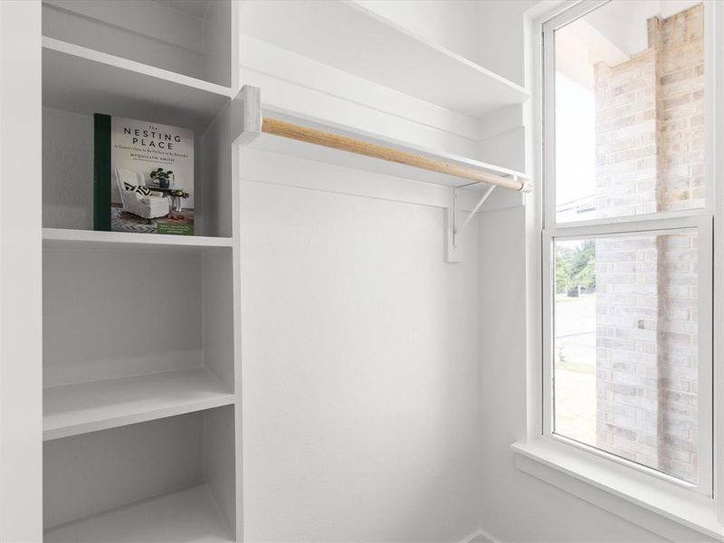 White closet shelving system featuring a wood-finish hanging rod, integrated shelving, and a bright window White closet shelving system featuring a wood-finish hanging rod, integrated shelving, and a bright window