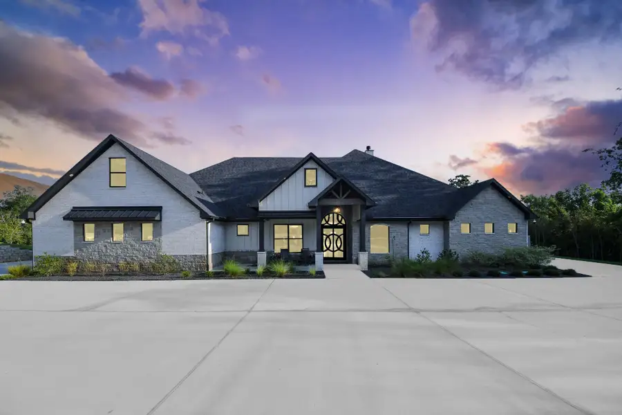 Stunning modern home with a spacious driveway, elegant stone facade, and inviting entryway set against a picturesque sunset.