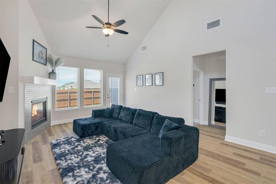 Living area featuring vaulted ceilings, wood-finish flooring, a contemporary fireplace with a tiled surround, a ceiling fan, and multiple windows providing natural light