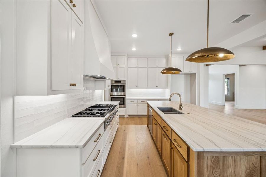 Kitchen featuring appliances with stainless steel finishes, custom exhaust hood, recessed lighting, light wood-style floors, and decorative backsplash Kitchen featuring appliances with stainless steel finishes, custom exhaust hood, recessed lighting, light wood-style floors, and decorative backsplash