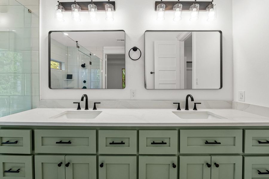 This bathroom features a double vanity with sleek black fixtures and dual square mirrors. The light green cabinetry adds a touch of color, complementing the contemporary design. Well-lit with stylish overhead lighting, it offers a fresh and inviting space. This bathroom features a double vanity with sleek black fixtures and dual square mirrors. The light green cabinetry adds a touch of color, complementing the contemporary design. Well-lit with stylish overhead lighting, it offers a fresh and inviting space.