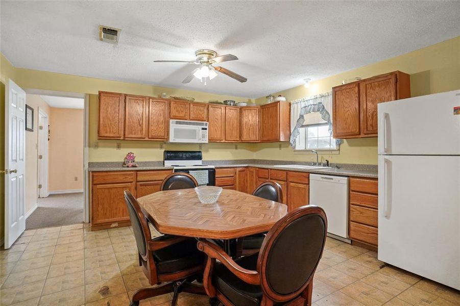 Kitchen with white appliances, a ceiling fan, brown cabinets, a textured ceiling, and light countertops