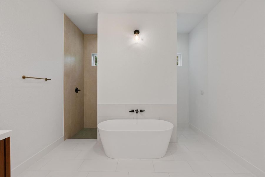 A freestanding soaking tub anchors this bathroom, complemented by a tiled walk-in shower and ample light.