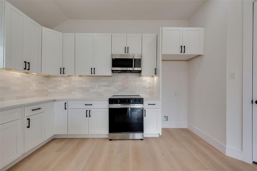 Kitchen with tasteful backsplash, white cabinetry, light wood-type flooring, and black range with electric cooktop