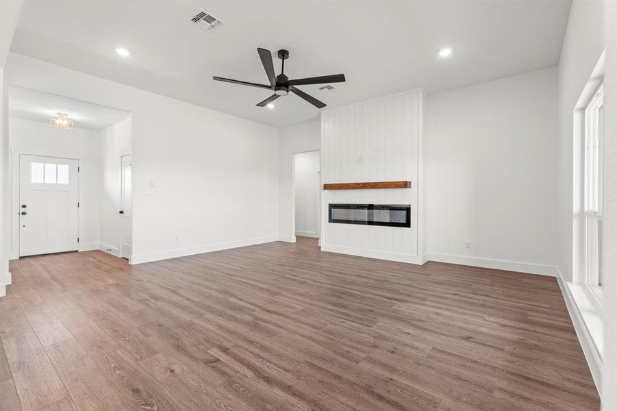 Unfurnished living room with wood finished floors, a ceiling fan, a large fireplace, and recessed lighting