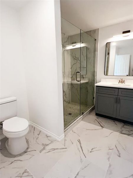 Bathroom featuring an enclosed shower with glass walls, a grey vanity with a white countertop, and patterned tile flooring