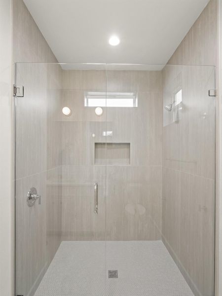 Walk-in shower featuring clear glass enclosure, neutral-toned large format tile walls, a built-in shower niche, and a honeycomb mosaic tile floor