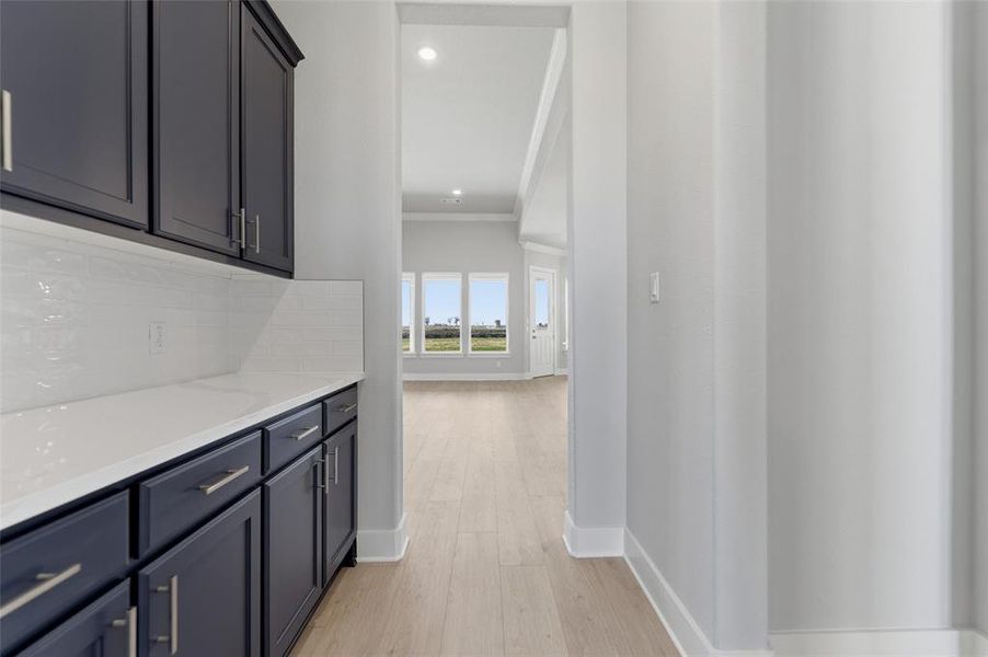 Bar area featuring light stone countertops, light wood finished floors, recessed lighting, crown molding, and backsplash
