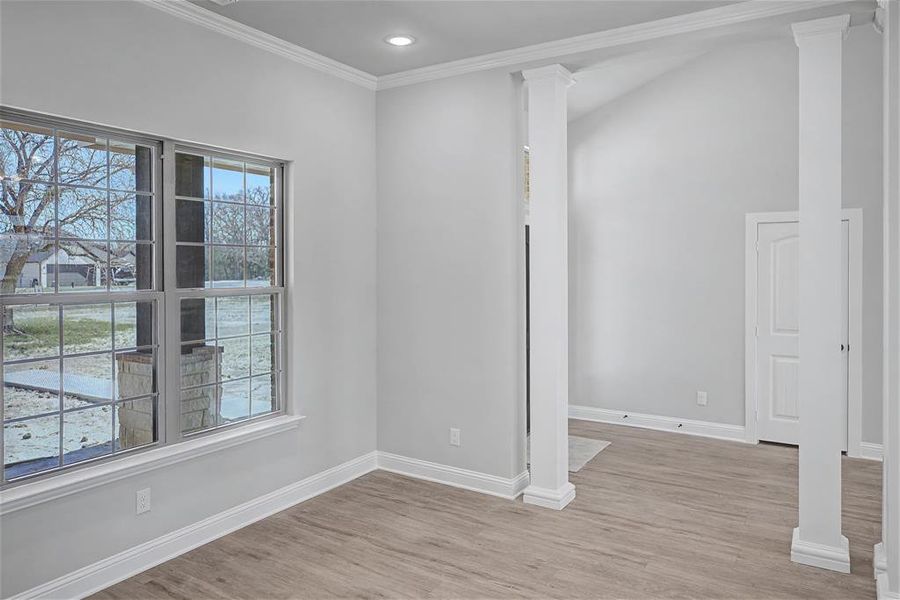 Empty room featuring ornate columns, crown molding, light wood-type flooring, and recessed lighting