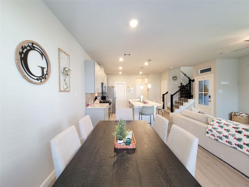 The room is well-lit, with neutral tones and stylish decor, creating an inviting atmosphere. A staircase leads to the upper floor, and large windows provide ample natural light.