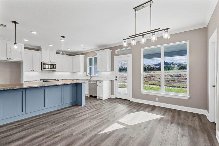 Kitchen featuring white cabinetry, hanging light fixtures, decorative backsplash, stainless steel appliances, and light stone counters