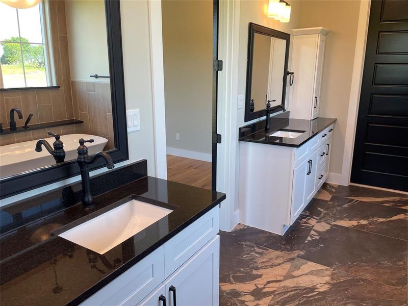 Dual vanity area featuring dark stone countertops, white shaker-style cabinetry, and matte black fixtures